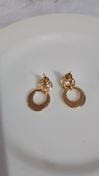 Yoniq.woman gold-tone circular drop earrings with polished finish and secure post-back closure on a white surface.