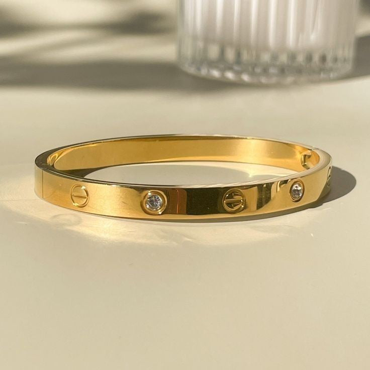 Yoniq.woman gold-tone metal bangle bracelet with crystal inlays and engraved screw-head motifs on a light surface.