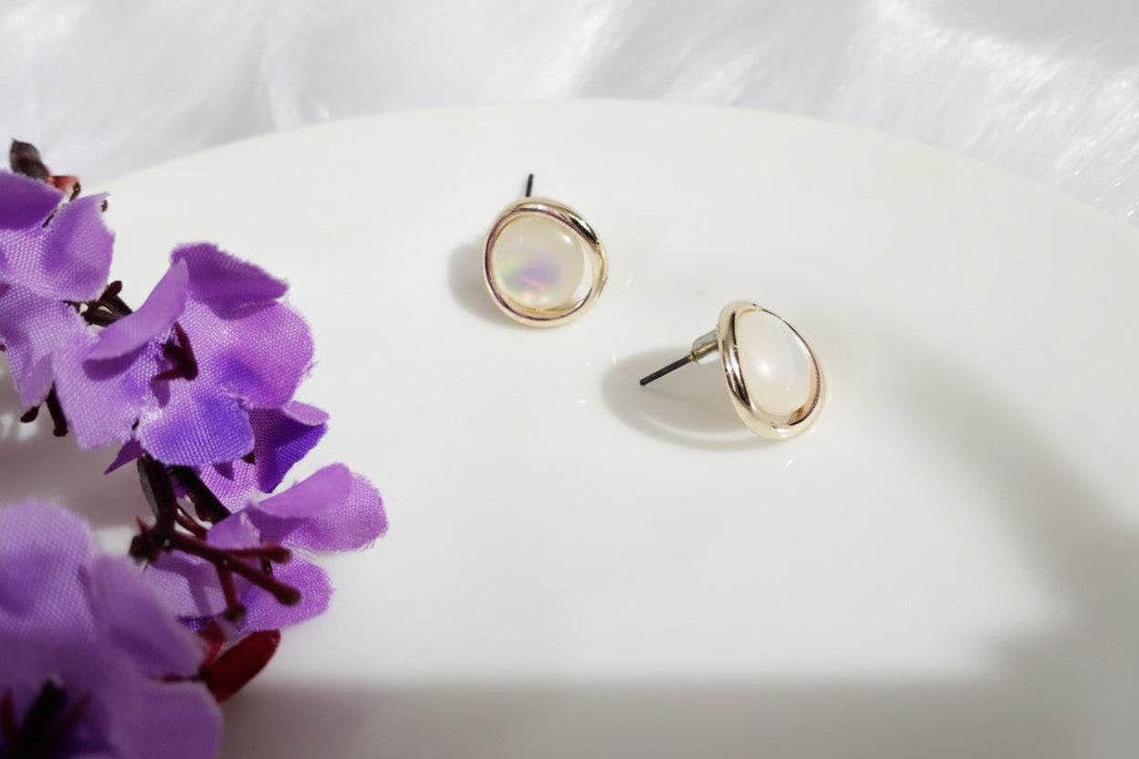 Yoniq.woman minimalist stud earrings featuring iridescent teardrop stones in polished gold-tone frames on a white plate.
