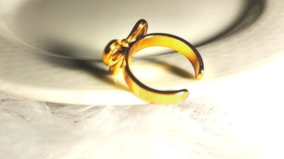 Yoniq.woman gold-tone adjustable bow ring with an open-back design resting on a white plate.