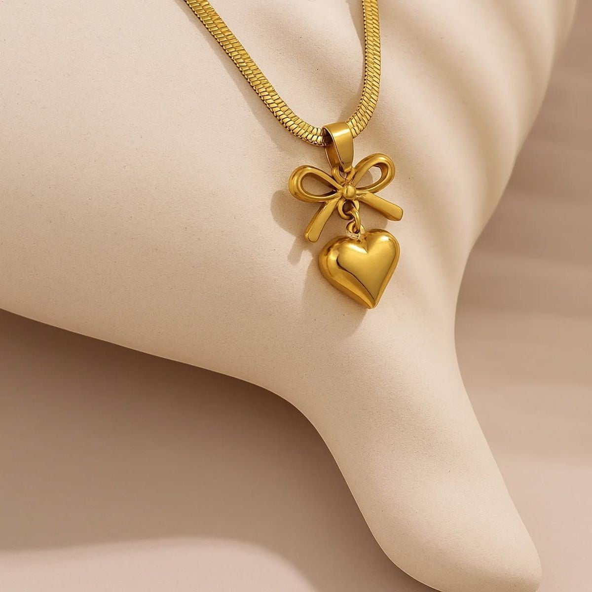 Yoniq.woman gold-tone necklace featuring a polished heart pendant suspended from a sculptural bow on a herringbone chain