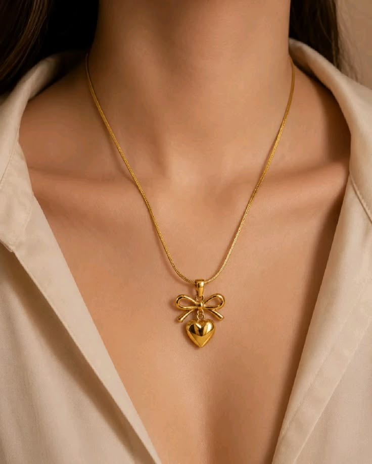 Yoniq.woman gold-tone necklace featuring a sculptural bow and heart pendant on a sleek herringbone chain