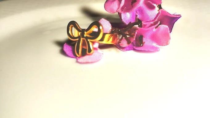 Yoniq.woman gold-tone adjustable finger ring featuring a dainty bow design resting on a purple flower petal
