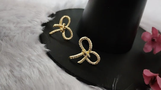 Yoniq.woman gold-tone bow stud earrings featuring a delicate twisted rope texture on a black display stand.