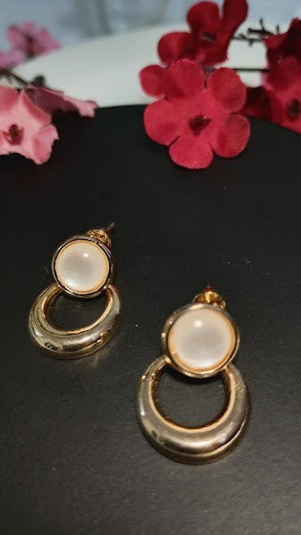Yoniq.woman gold-tone circular drop earrings with smooth white cabochon studs on a black display surface