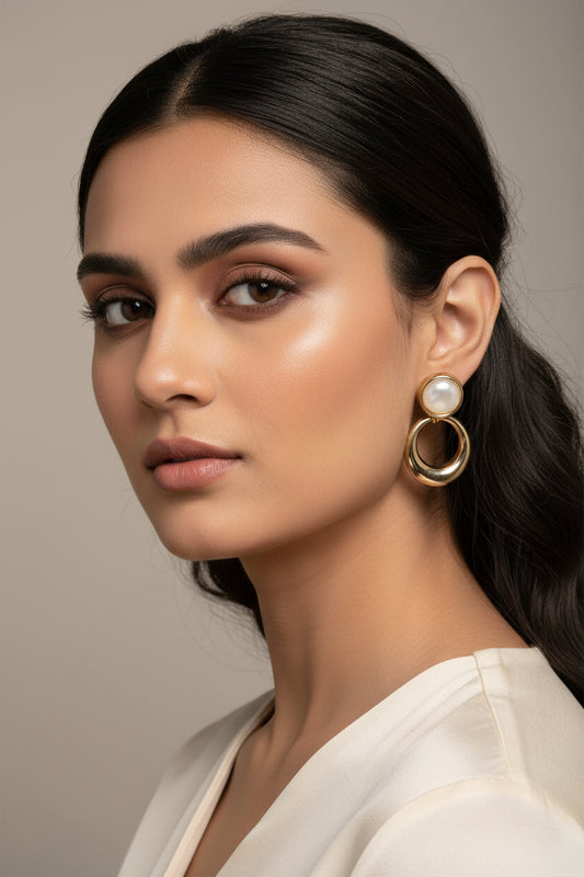 Yoniq.woman gold-tone circular drop earrings with white cabochon studs on a black display with pink flowers