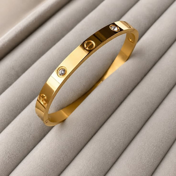 Yoniq.woman gold-tone metal bangle bracelet with screw-head motifs and sparkling crystal inlays on a grey display