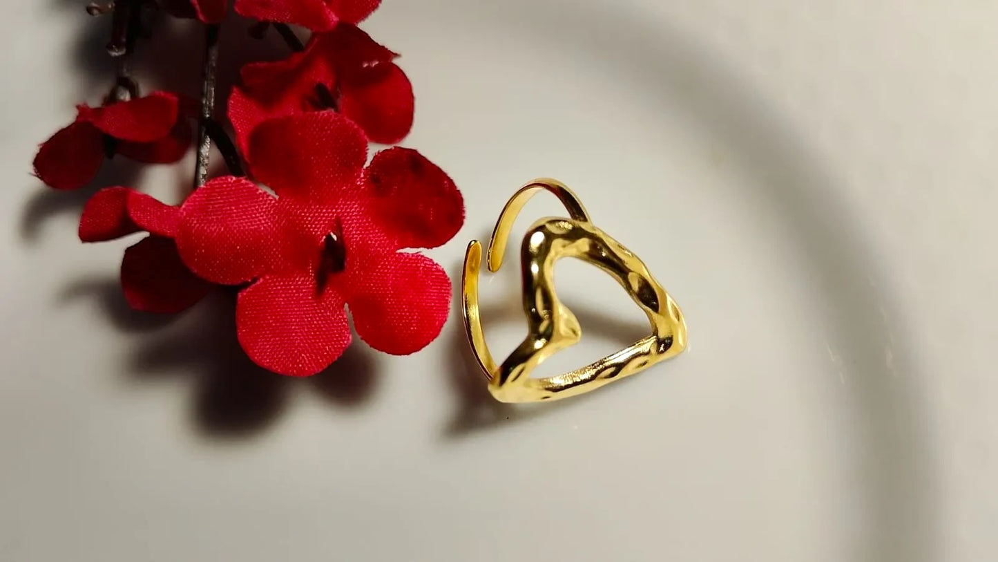 Yoniq.woman gold-tone open heart ring with a hammered texture, resting on a white surface next to red flowers.