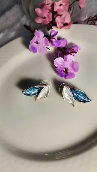 Yoniq.woman leaf-shaped stud earrings featuring blue and white enamel with gold-toned edges on a white plate.