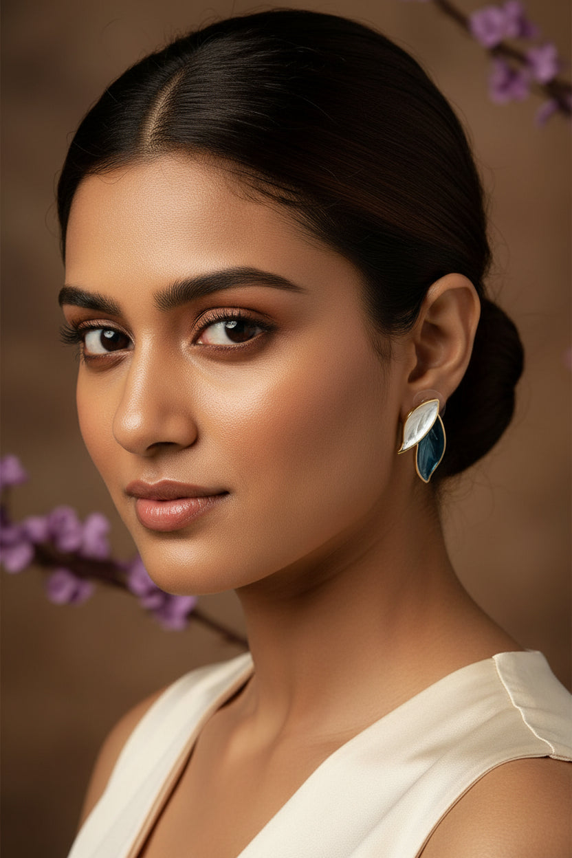 Yoniq.woman leaf-shaped stud earrings in blue and white enamel with gold-toned edges on a floral background