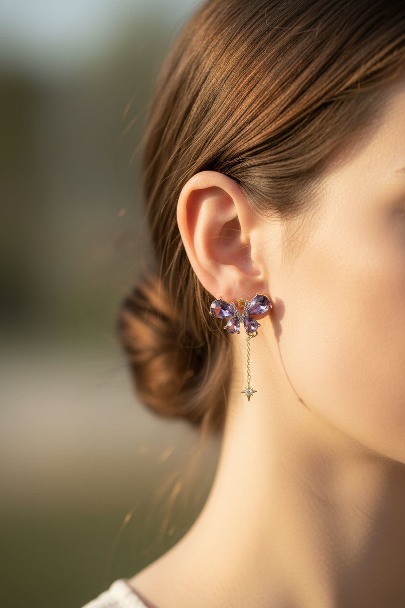Yoniq.woman butterfly stud earrings with purple teardrop crystals, gold-tone setting, and dangling star charms.
