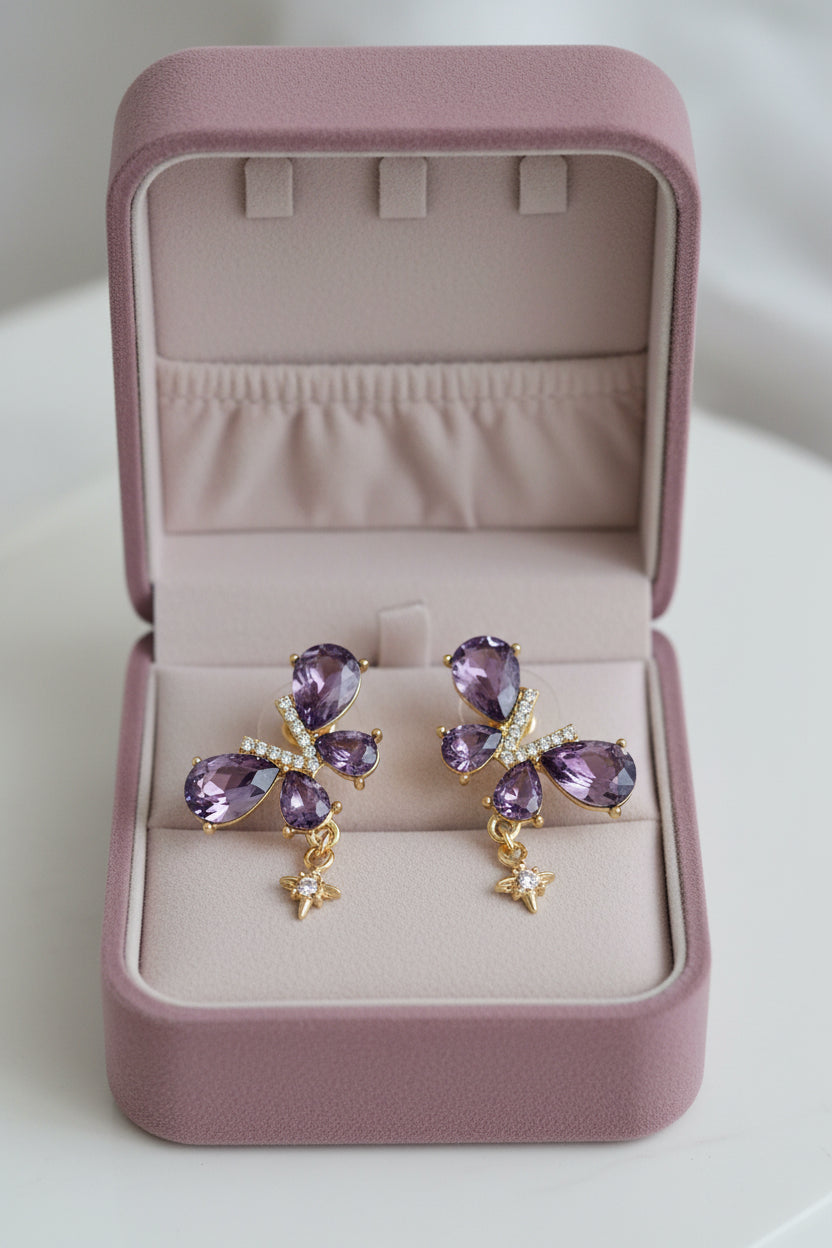 Yoniq.woman butterfly stud earrings with purple teardrop crystals, gold-tone setting, and dangling star charms.