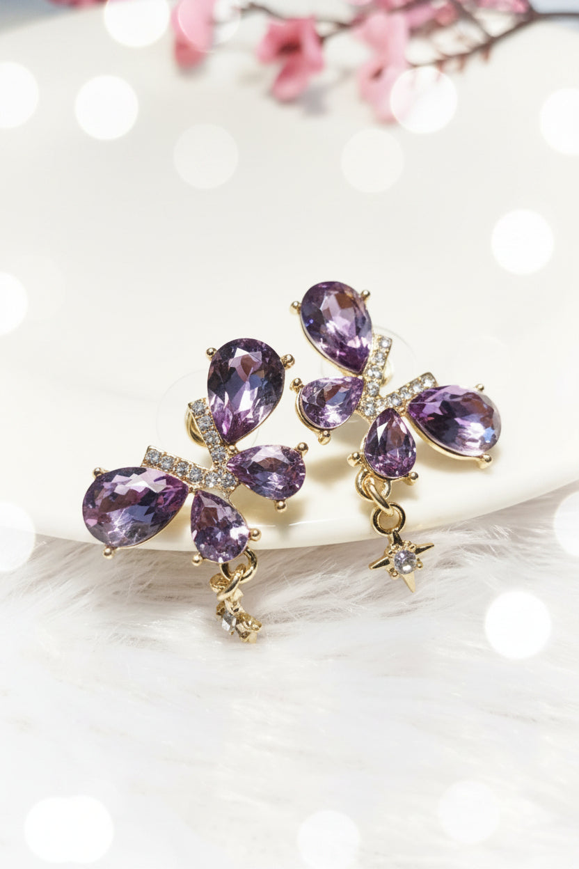 Yoniq.woman butterfly stud earrings with purple teardrop crystals, gold-tone setting, and dangling star charms.