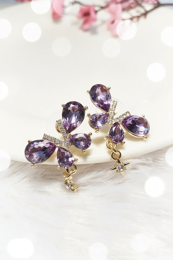 Yoniq.woman butterfly stud earrings with purple teardrop crystals, gold-tone setting, and dangling star charms.