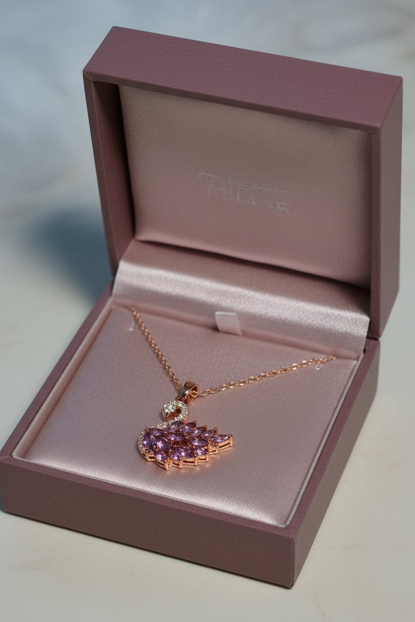Yoniq.woman rose gold swan pendant necklace with purple marquise-cut crystals and pavé detailing on a white surface.