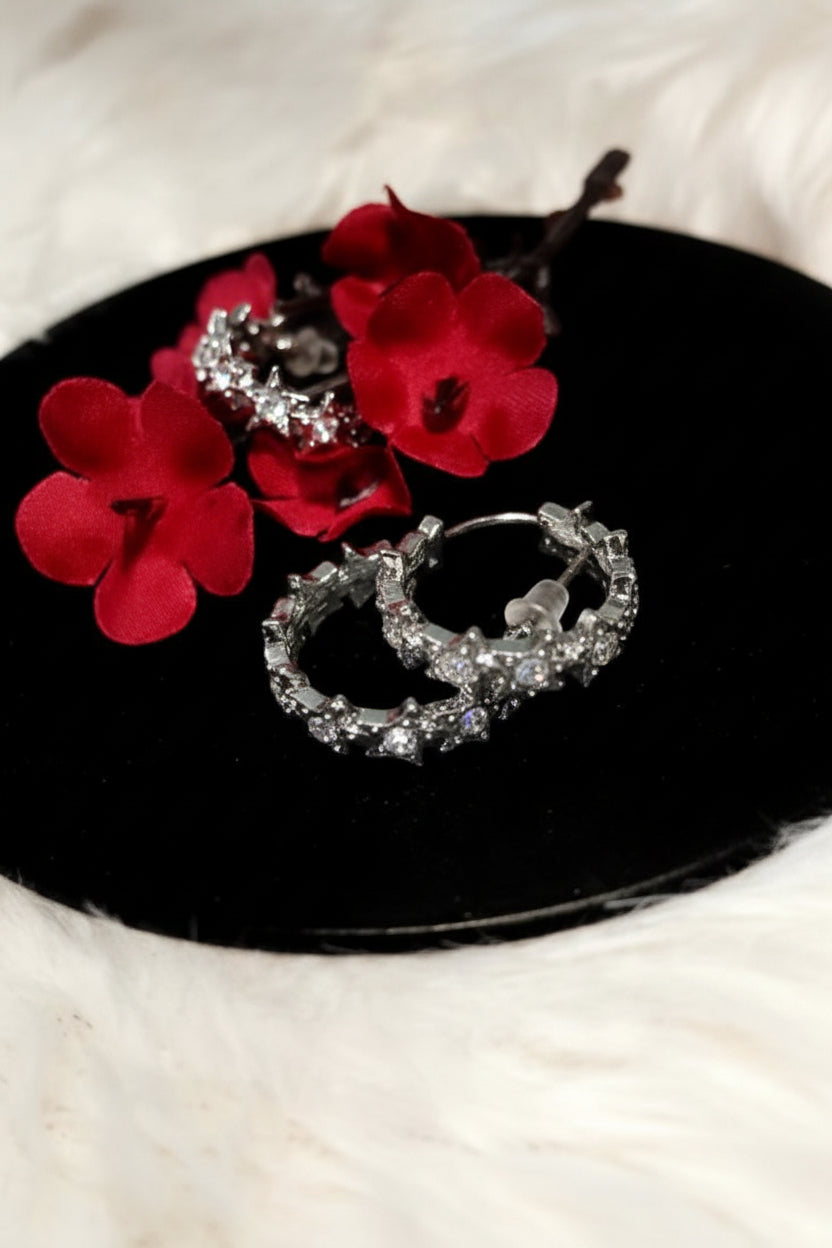 Yoniq.woman silver-tone hoop earrings featuring a row of sparkling star motifs with clear crystals on a black base.